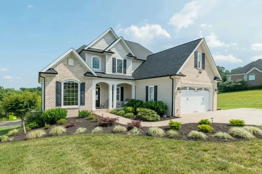 Two-story stone and siding home with a landscaped front yard