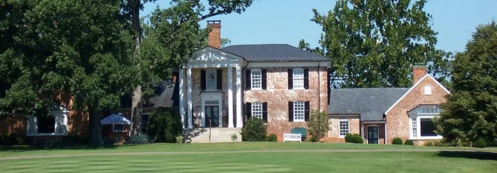 Brick colonial home with white columns behind a green lawn