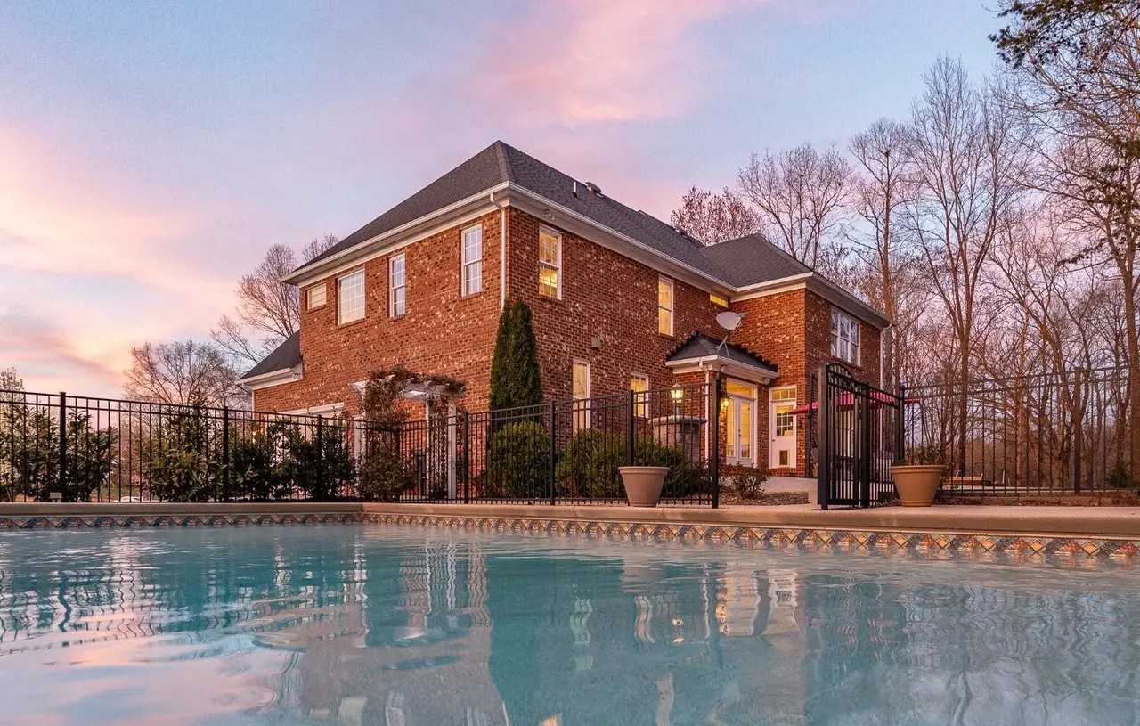 A two-story brick home in Forest, VA, seen across its swimming pool at sunset.