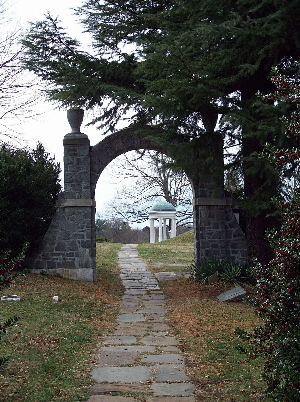 A stone arch and flagstone path at Old City Cemetery, with a white gazebo beyond