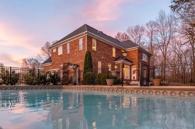 Pool with a black iron fence and the brick house beyond at sunset at 1108 Half Moon Court, Forest VA