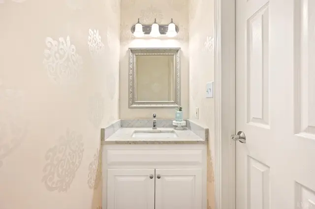 Powder room with a white vanity and patterned wallpaper at 1351 Country Estates Drive, Lowry VA