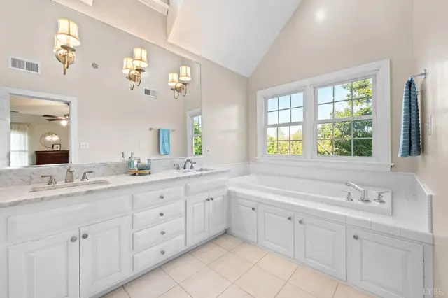 Bathroom with a double vanity, brass sconces and a soaking tub at 1351 Country Estates Drive, Lowry VA