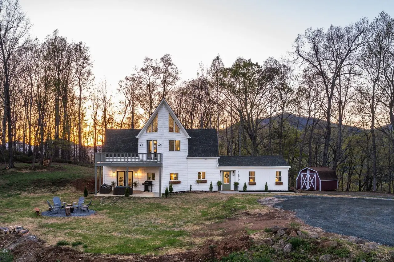 Front of the white farmhouse with a balcony and a red shed at dusk at 1520 Grassy Mountain Lane, Forest VA