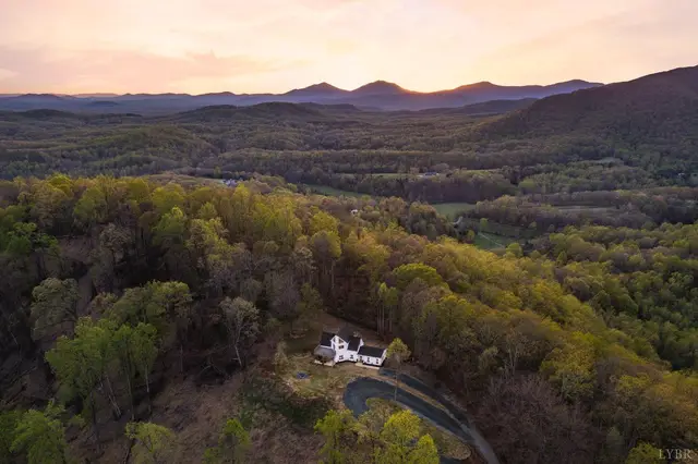 Aerial view of the house in a wooded valley with mountains at sunset at 1520 Grassy Mountain Lane, Forest VA