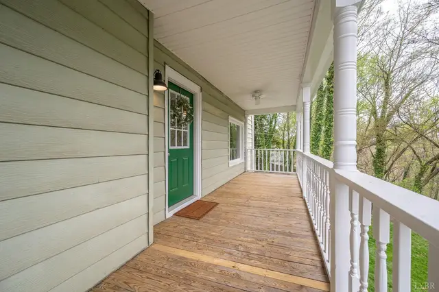 Covered front porch with wood floors, white railings and a green door at 223 7th Street, Madison Heights VA