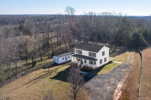 Aerial view of the two-story white house on a wooded lot with a pasture at 2389 New Chapel Road, Rustburg VA