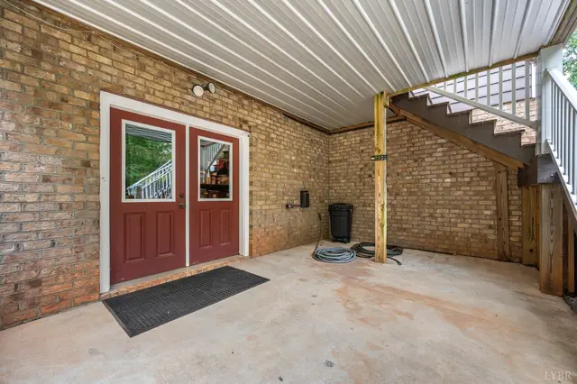 Covered patio under the deck with red double doors and brick walls at 2842 Chilton Road, Appomattox VA