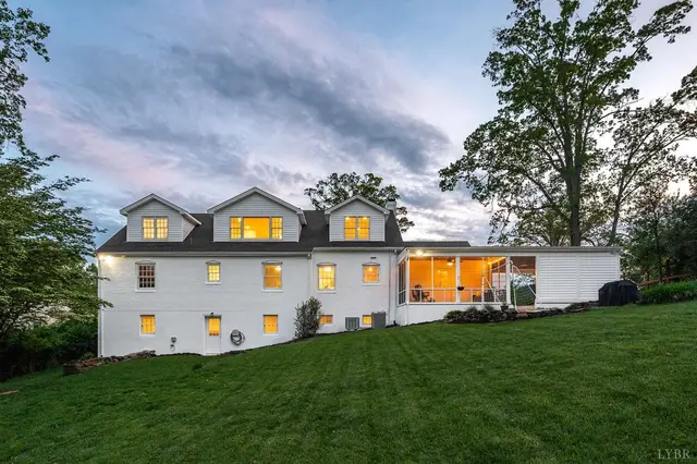 Side view of the white house with dormers and a lit sunroom at 3760 Woodside Avenue, Lynchburg VA