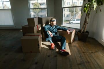 Man in denim sitting in empty room with packed moving boxes